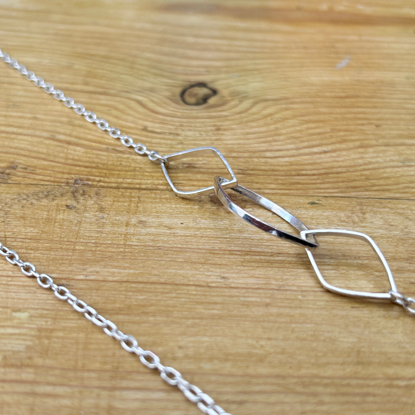 A close up of the leaf links of the elegant statement sterling silver necklace - displayed on a wooden surface