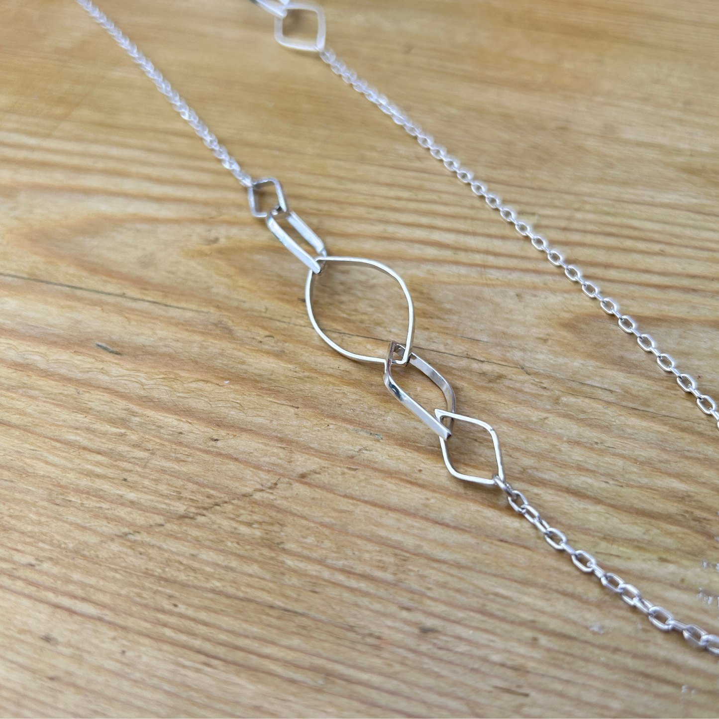 A handmade elegant sterling silver leaf link necklace laid on a natural wood surface - a close up of the leaf links