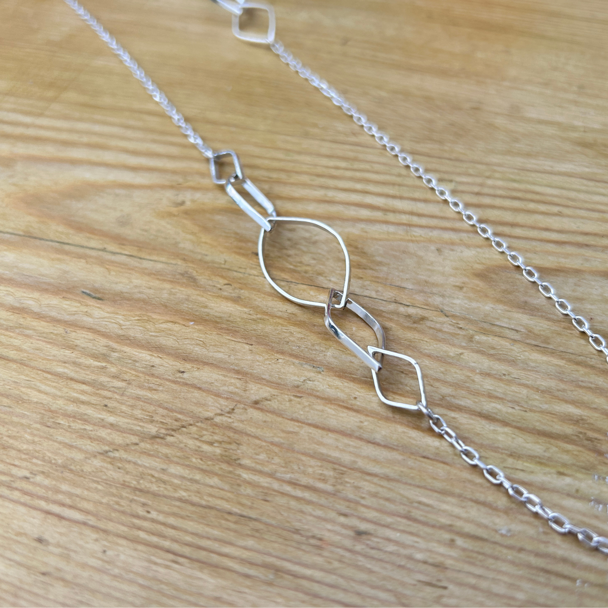 A handmade elegant sterling silver leaf link necklace laid on a natural wood surface - a close up of the leaf links