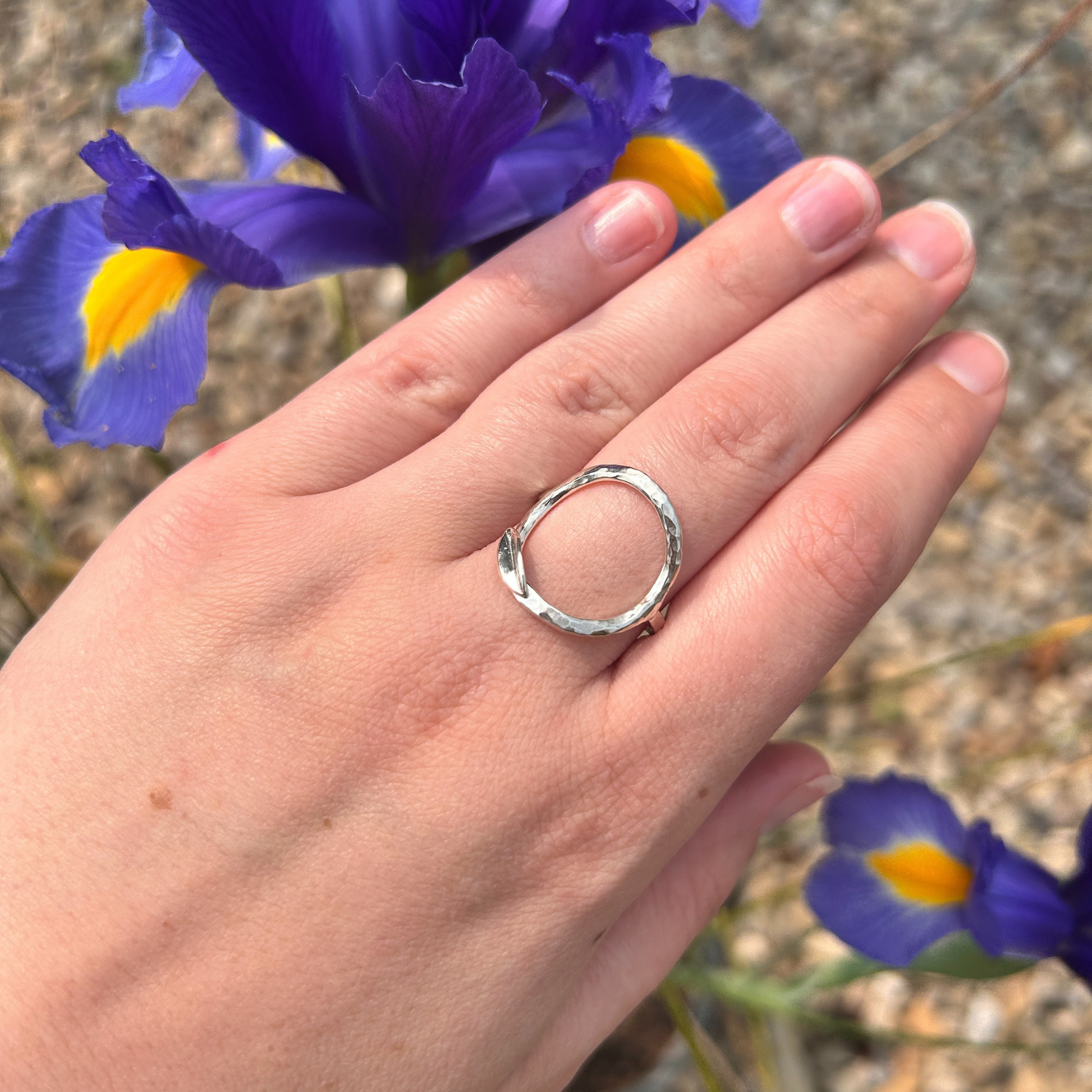Hand wearing a hammered open circle silver ring with blooming purple irises in the background