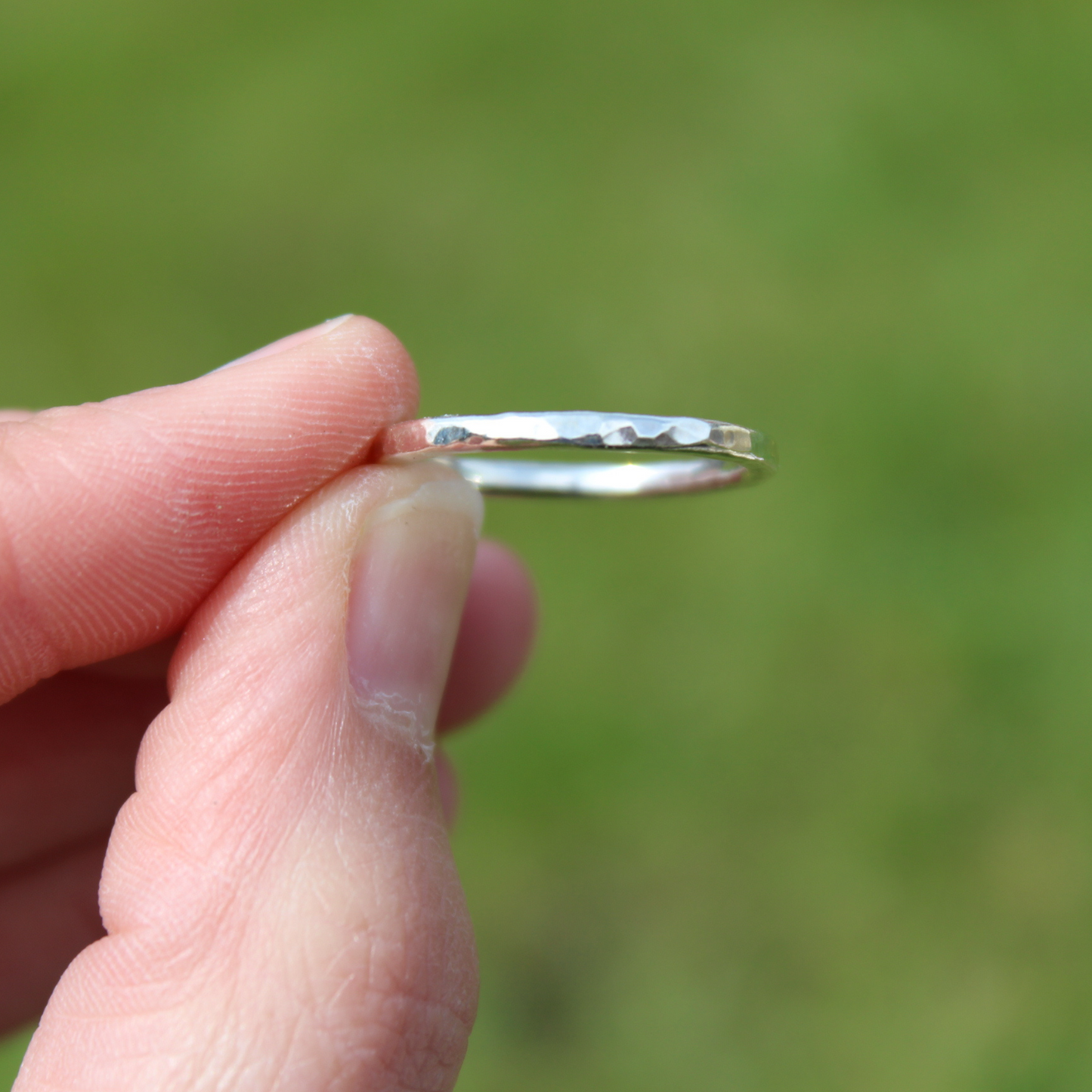 Handmade 2mm sterling silver hammered ring - held in pinched fingers against a green background