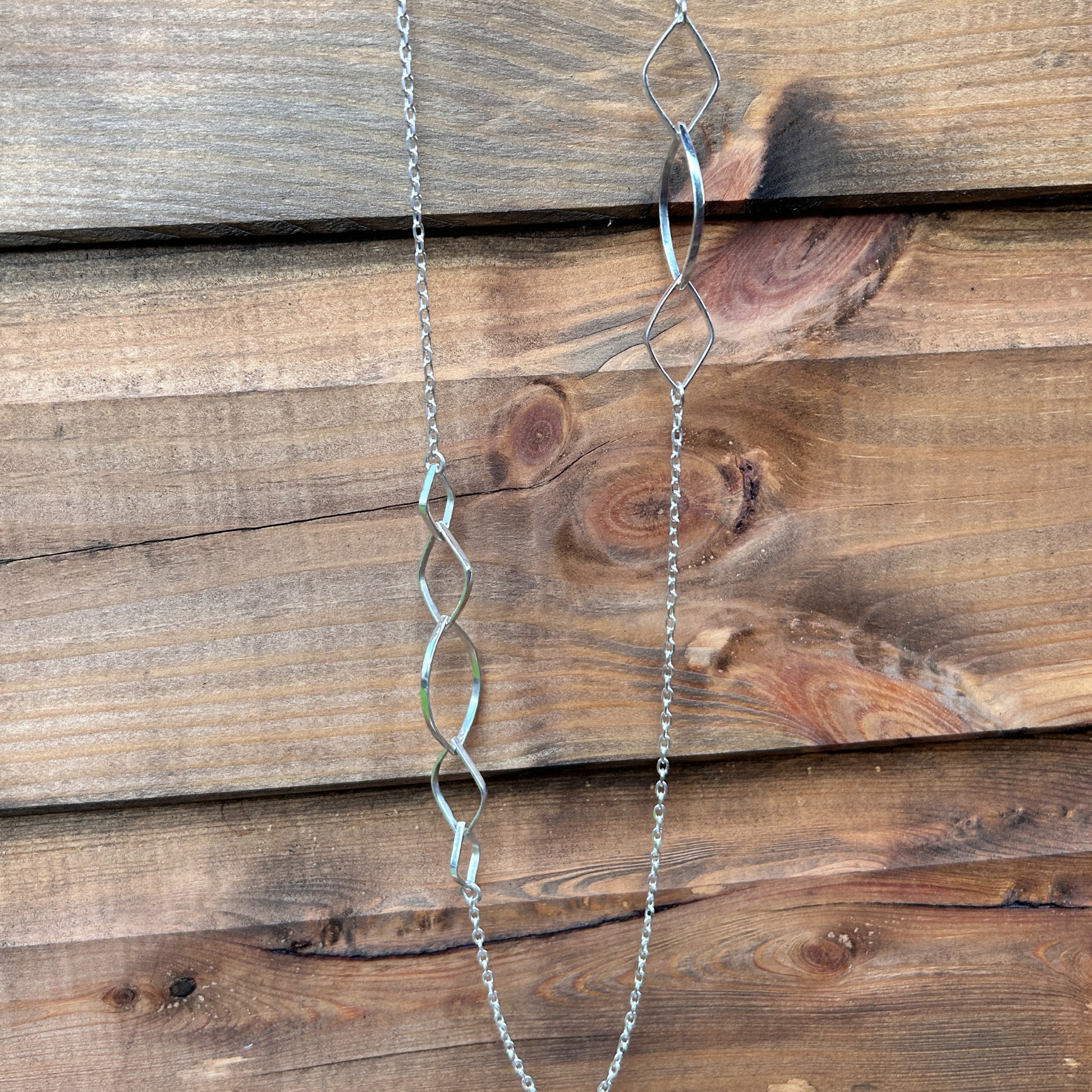 Refined sterling silver asymmetrical designer necklace featuring interlocking leaf-shaped links on a delicate chain, elegantly displayed on a polished wooden surface.
