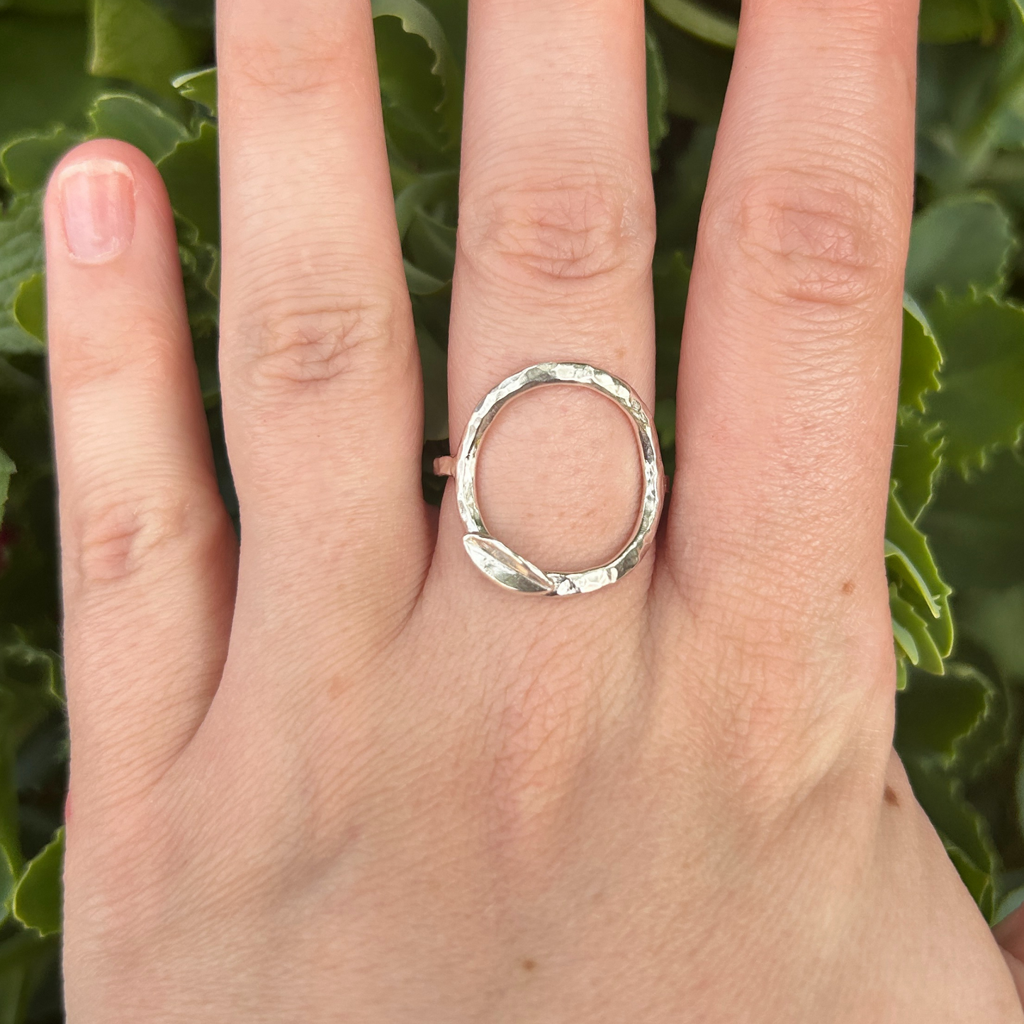 Hand wearing a hammered open circle silver ring with succulent in the background