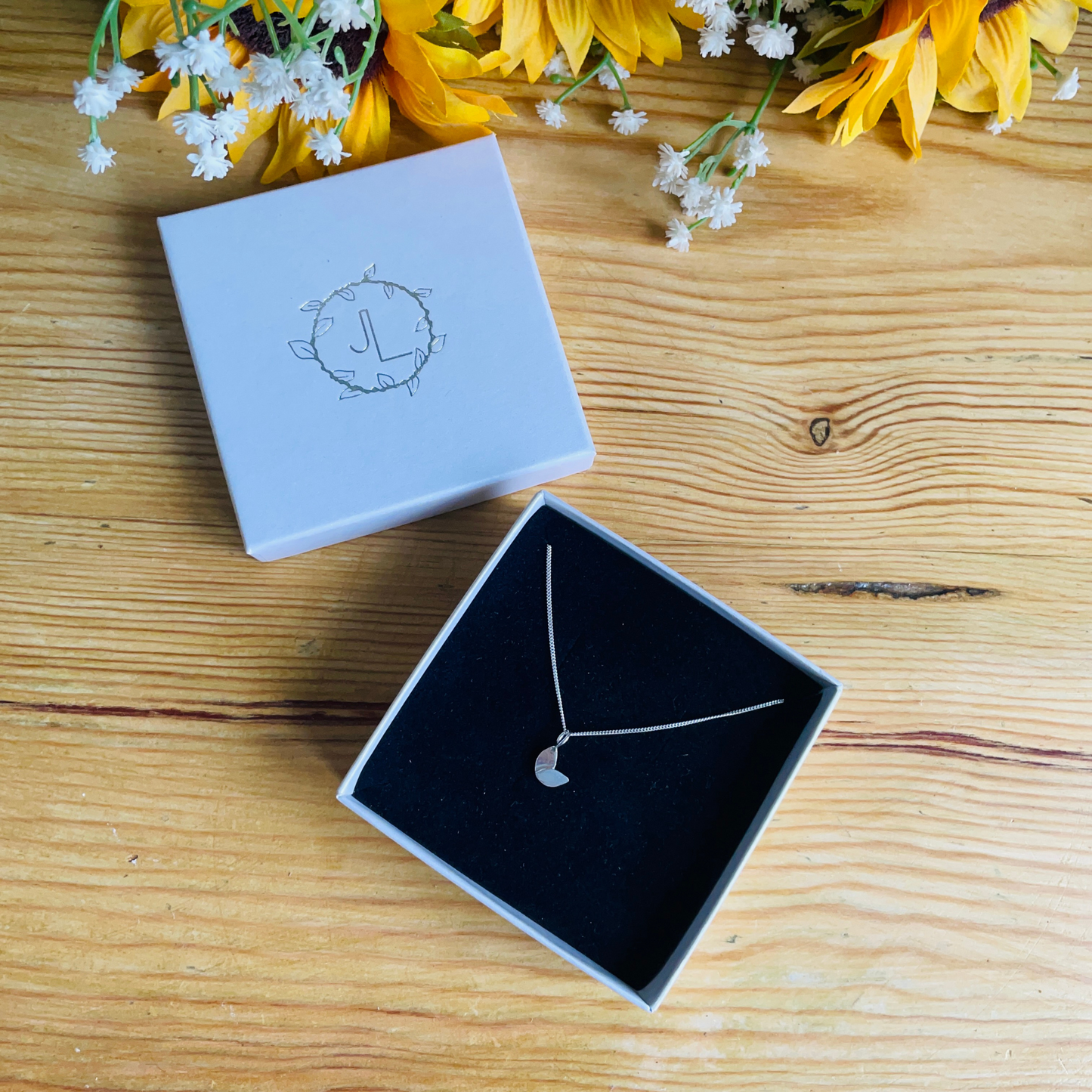 a small sterling silver duo leaf necklace in an ivory box with black velvet insert on wooden background - handmade by Jen Lithgo Jewellery