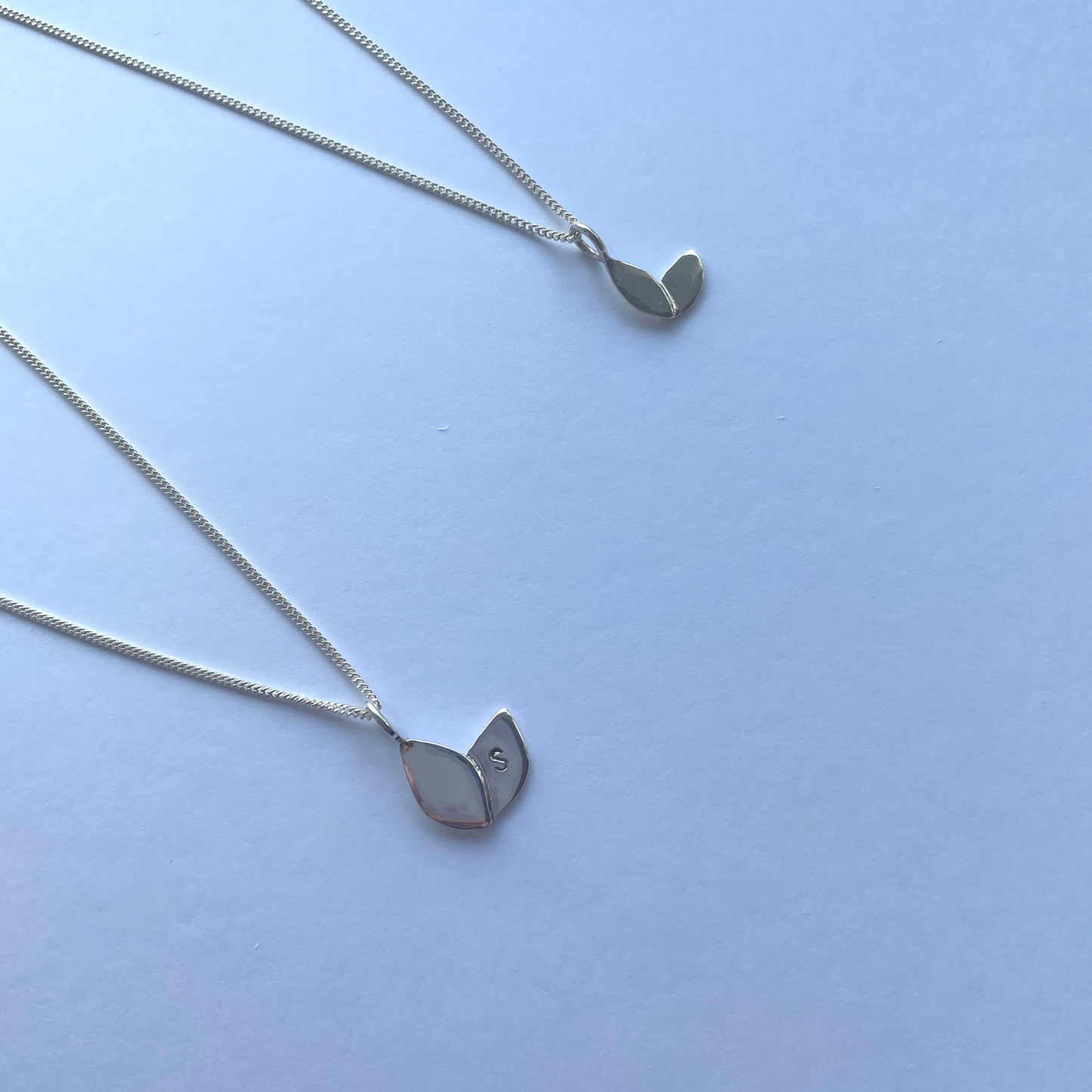 two silver necklaces with leaf shaped pendants laid on a white background. Large pendant is hand stamped with an "S". Handmade by Jen Lithgo Jewellery
