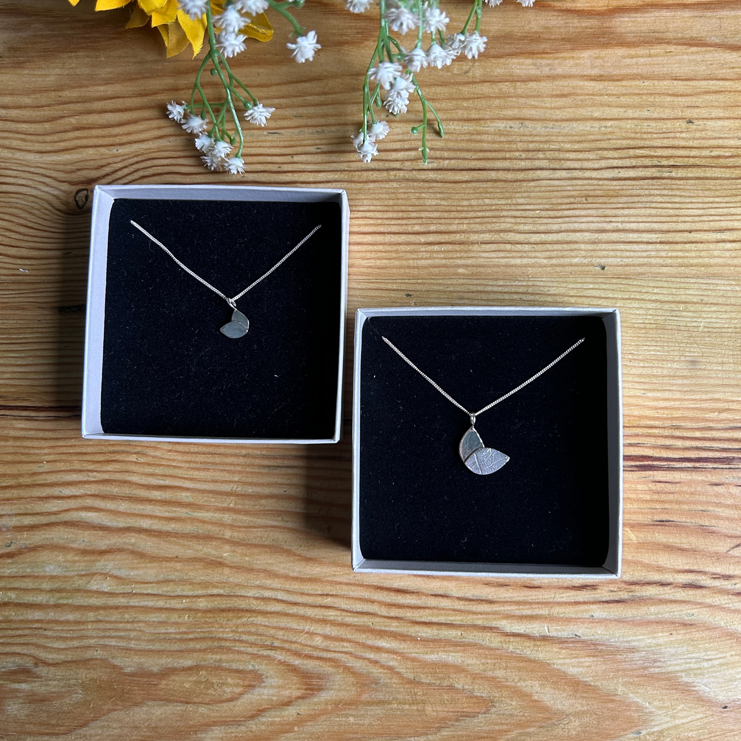 two handmade duo leaf necklaces in two sizes in ivory boxes with black insert on a wooden table top. Made from Sterling Silver by Jen Lithgo Jewellery