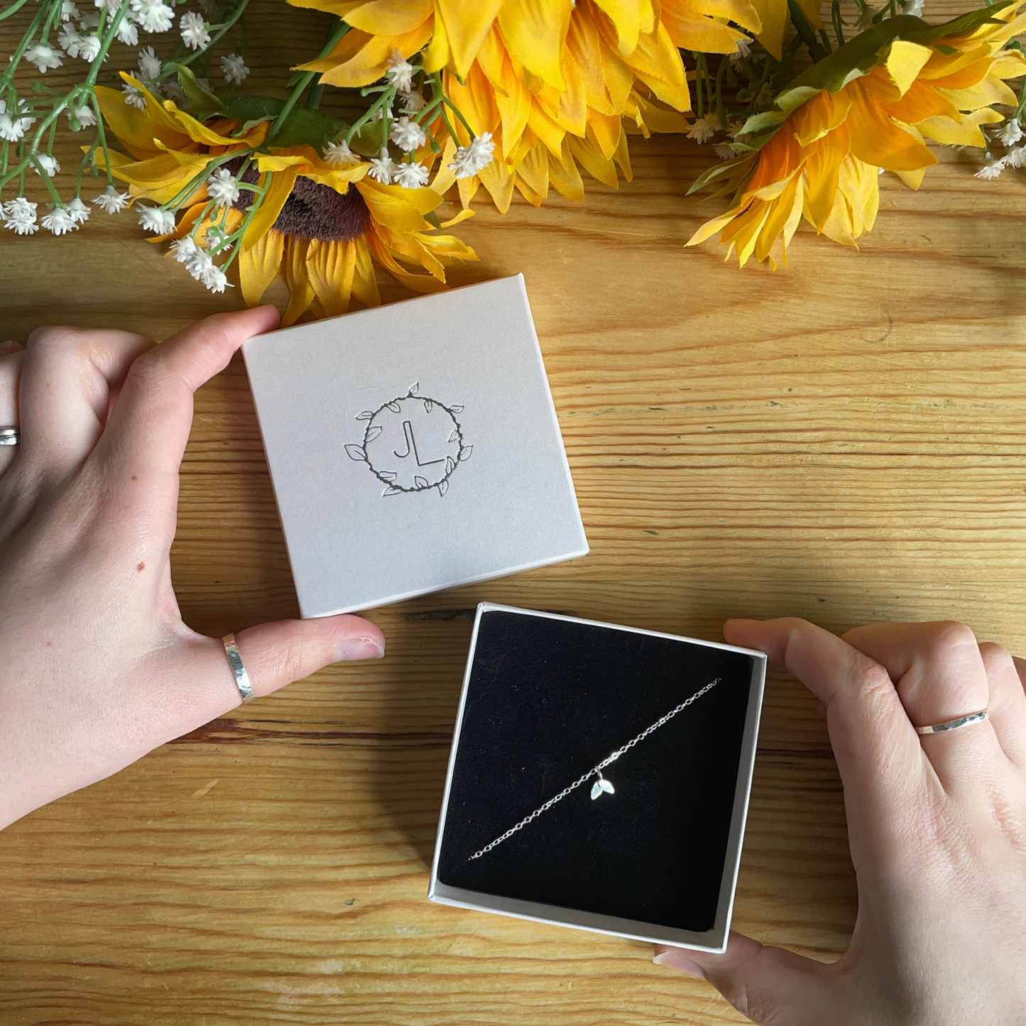 duo leaf bracelet in an ivory box being held infront of a wooden backdrop with sunflower