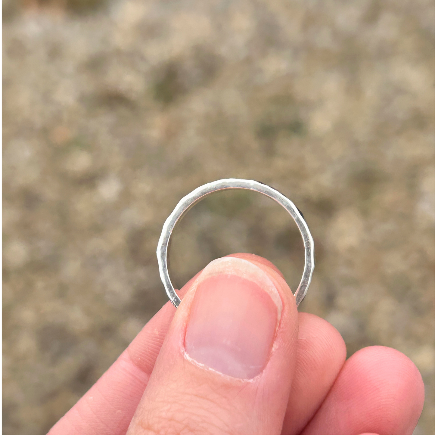 Recycled Sterling Silver ring held between fingers with a blurred natural background