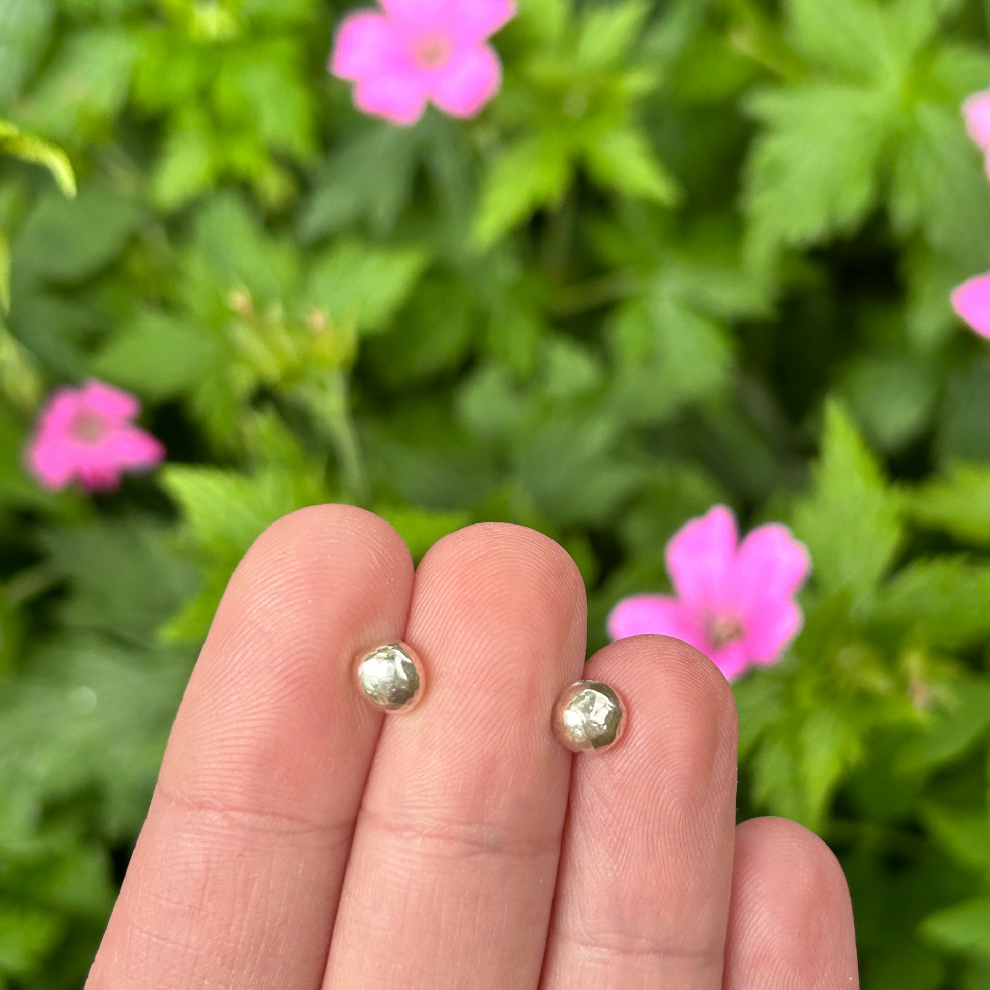 Large sterling silver handmade pebble stud earrings held in a hand against a pink and green floral background