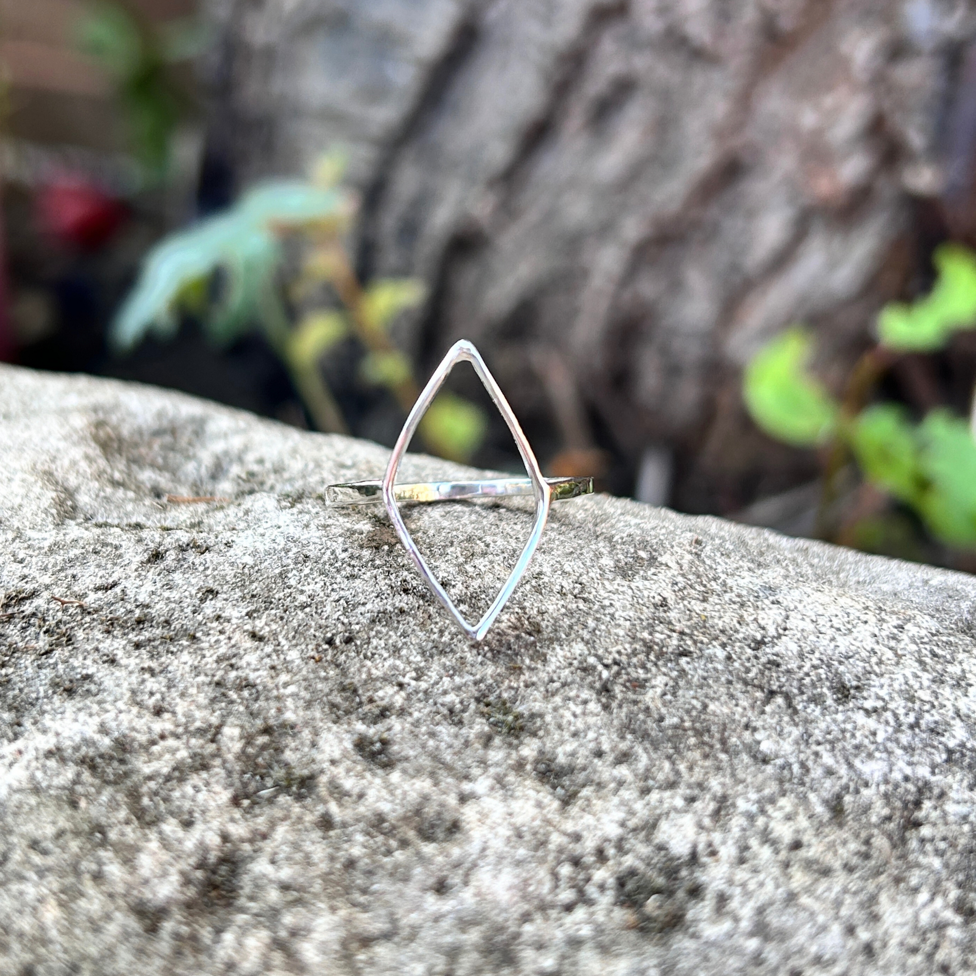 A handmade sterling silver geometric open leaf ring on a textured stone surface with a natural background