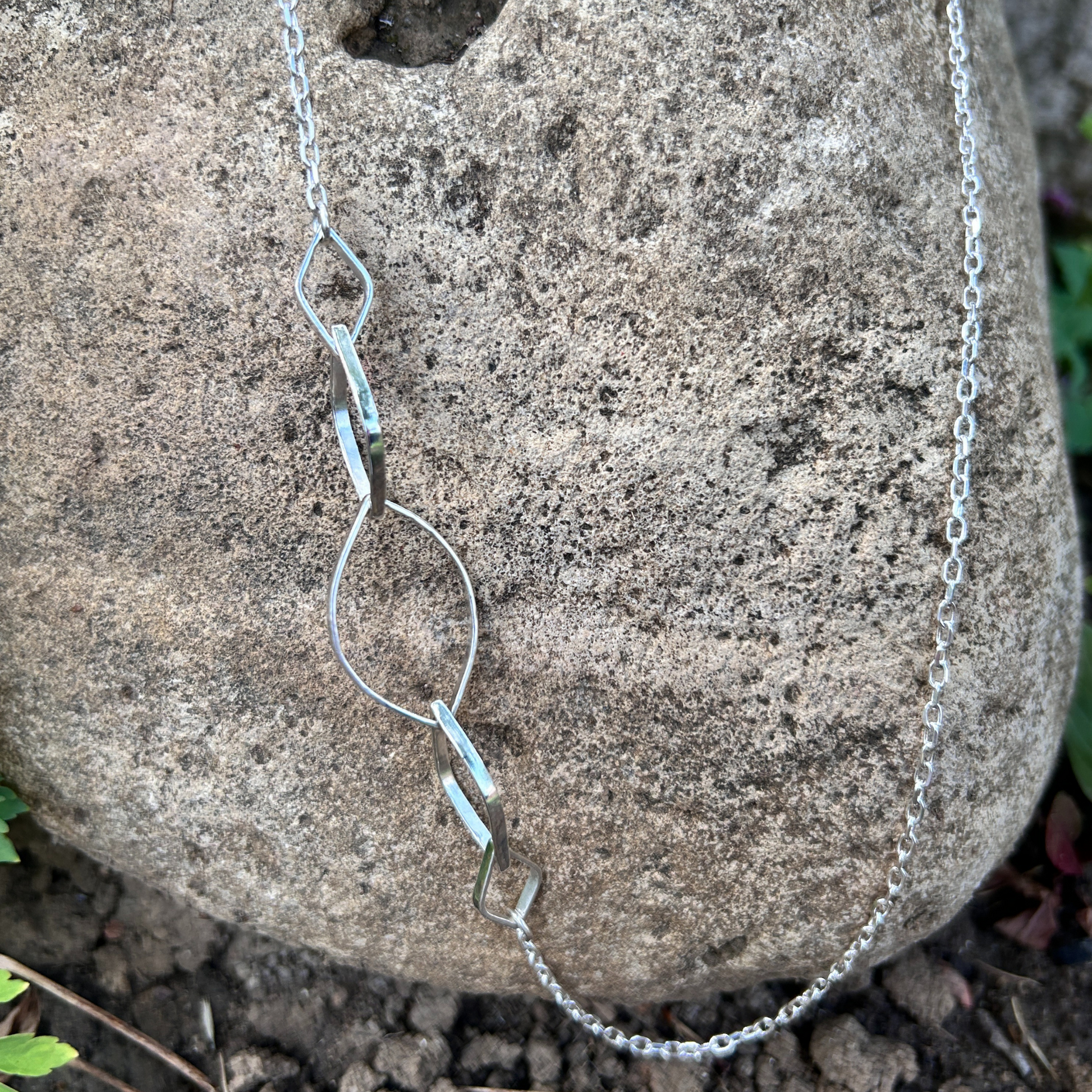 Refined sterling silver asymmetrical designer necklace featuring interlocking leaf shaped links on a delicate chain, elegantly draped over a rock