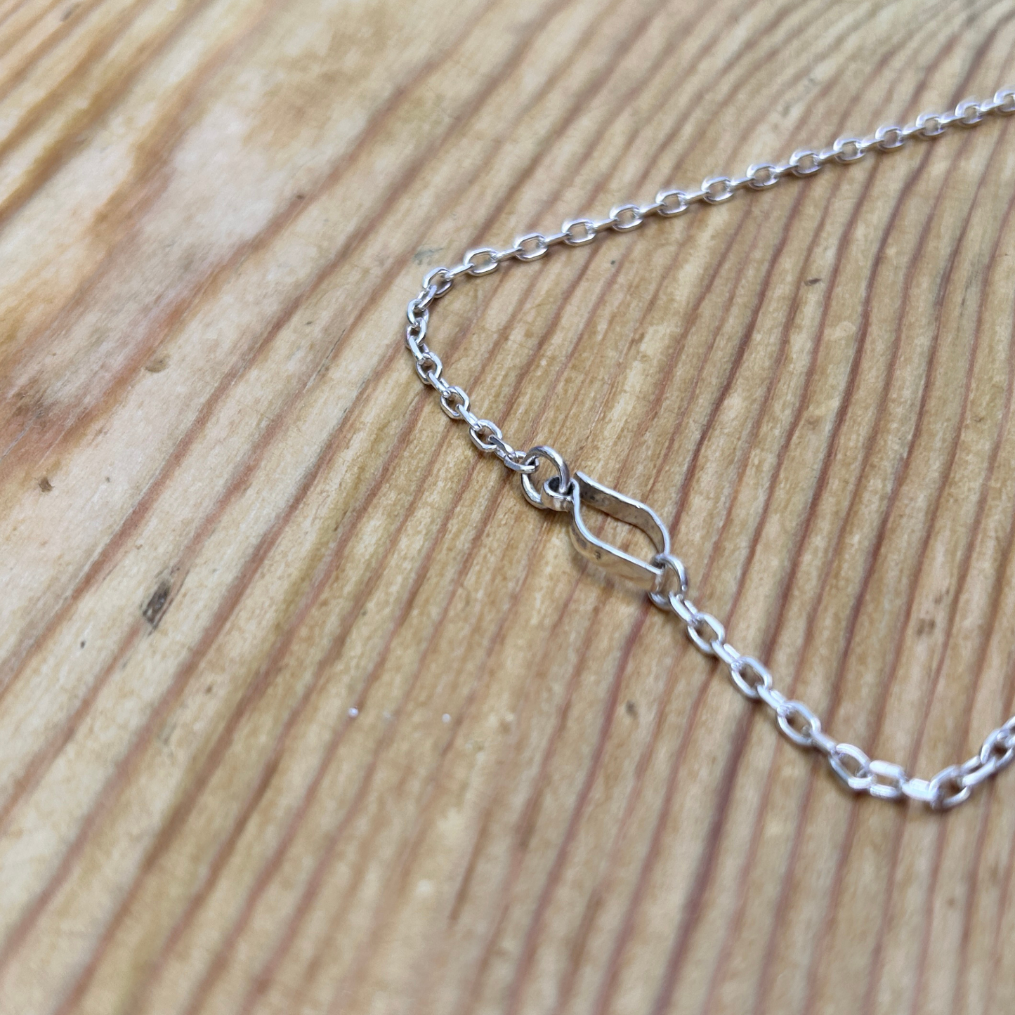 A close up of the catch on an elegant sterling silver necklace with interlocking marquise-shaped links displayed on natural wood surface