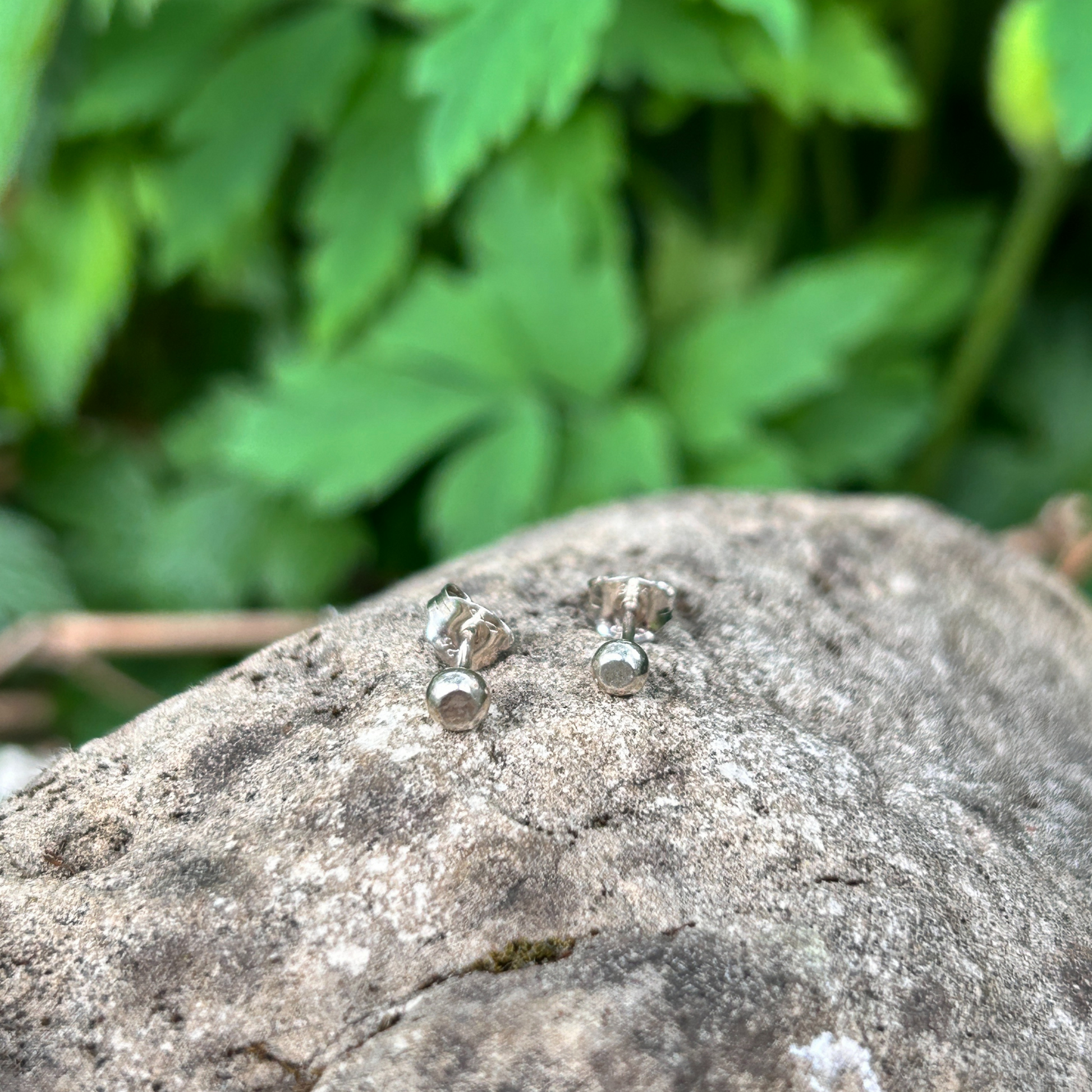 Silver small pebble stud earrings sat on a rock - handmade nature jewellery
