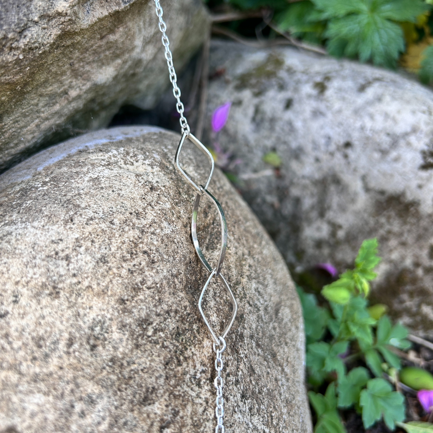 Elegant sterling silver necklace with interlocking marquise-shaped links displayed on natural stone background with green foliage - close up of the leaf links