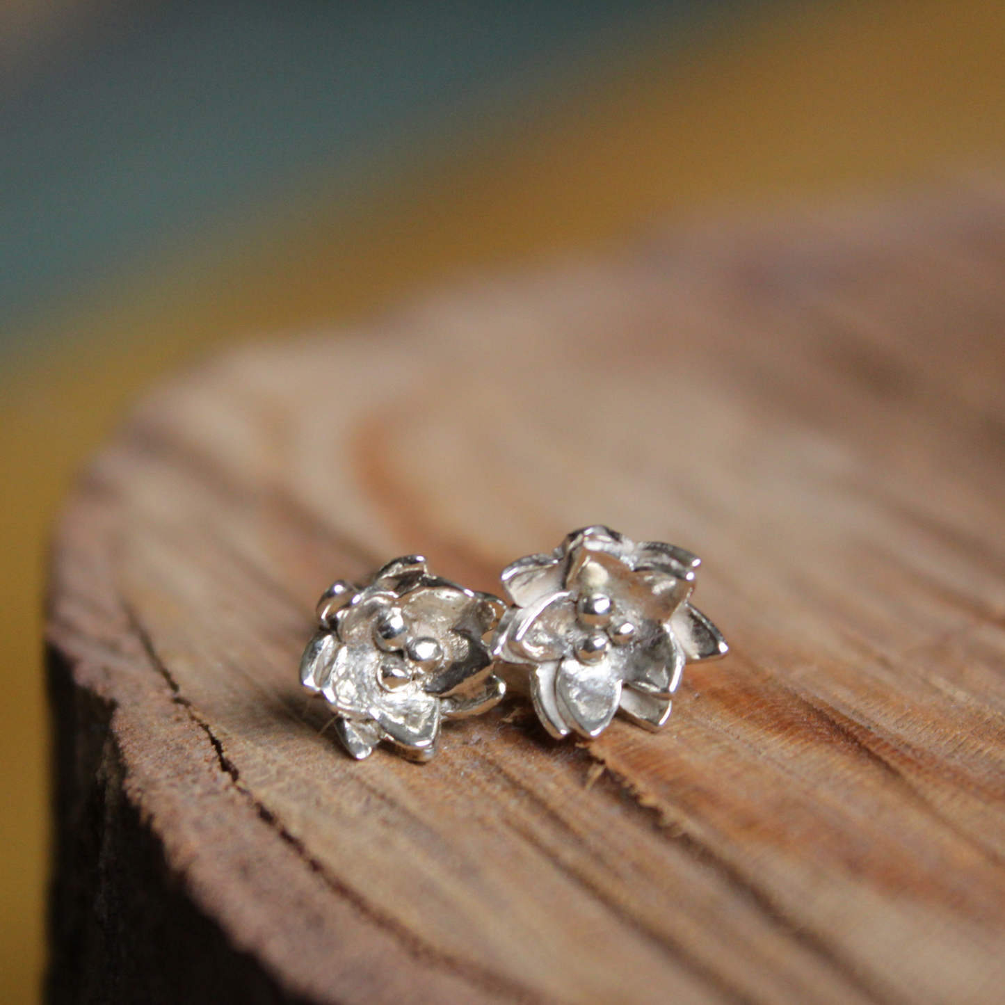 A pair of sterling silver flower studs sitting on a tree stump - handmade by Jen Lithgo Jewellery