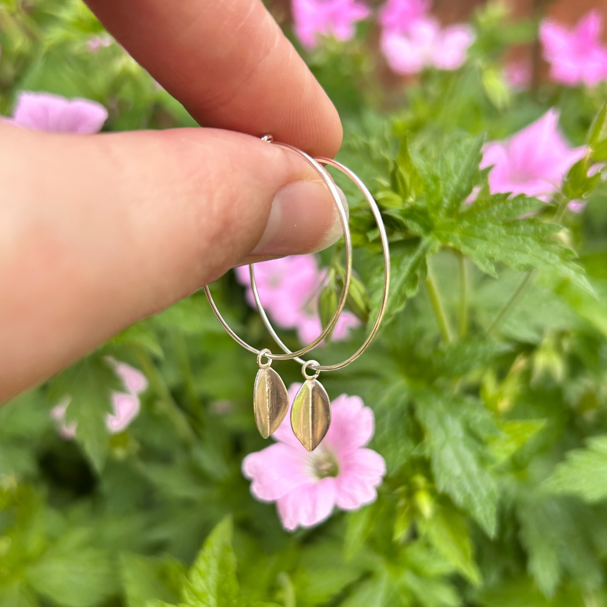 A hand holding a wire hoop with a leaf hanging from each earring.