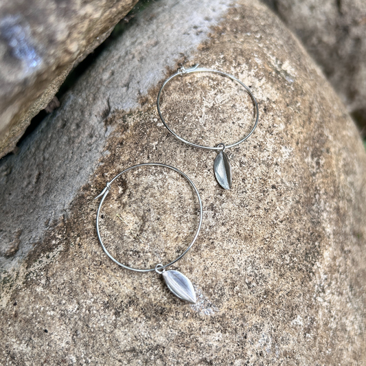 Wire hoop earrings laid on a stone background with a silver leaf hanging from each hoop.