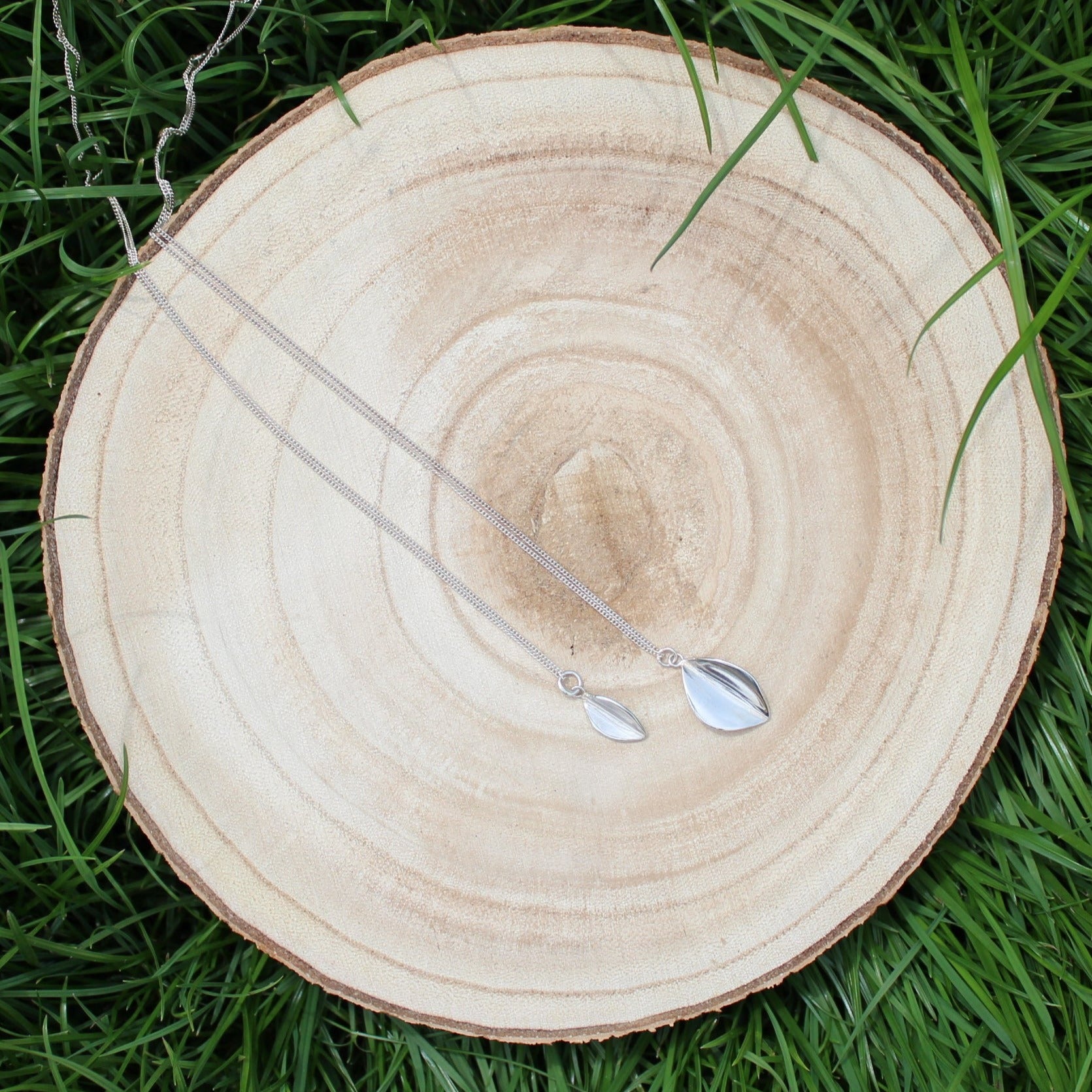 Large and Small Leaf Necklace laid on wooden log in the grass, Handmade in Sterling Silver by Jen Lithgo Jewellery