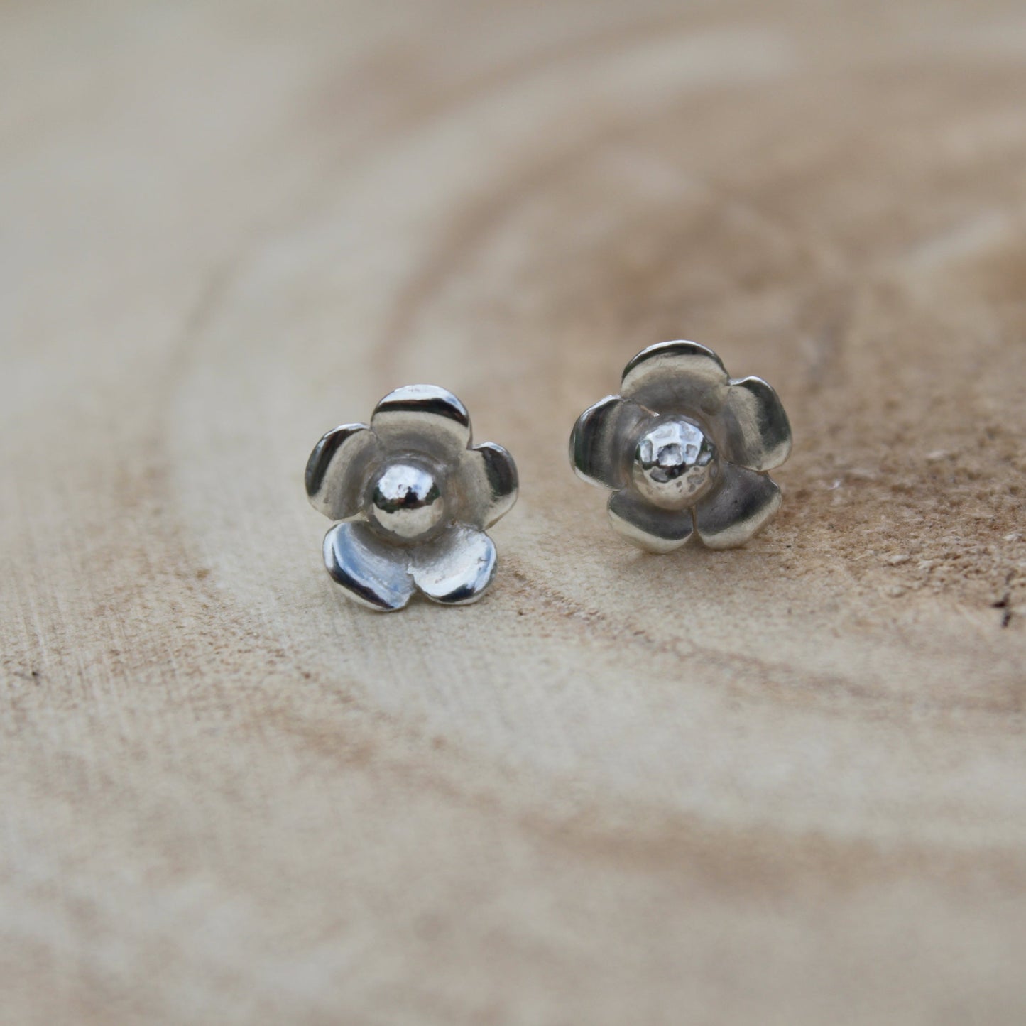 A pair of silver flower studs on a wooden background