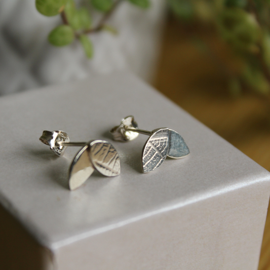 A pair of two leaf stud earrings sat on top of an ivory box. One leaf on each stud is printed with a leaf vein pattern. Handmade by Jen Lithgo Jewellery