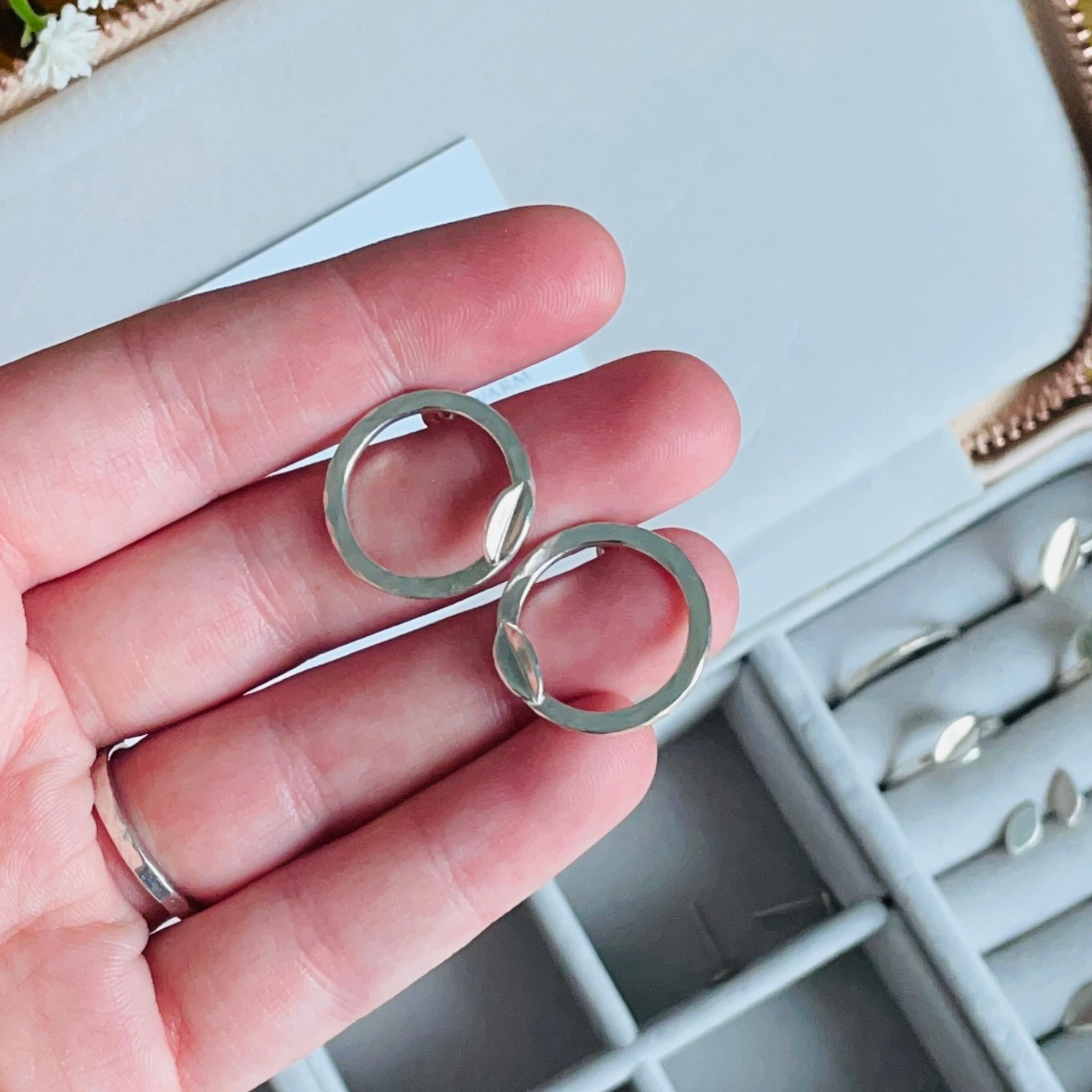 Handmade sterling silver stud earrings with hammered texture and folded silver leaves beng held by a womans hand. By Jen Lithgo