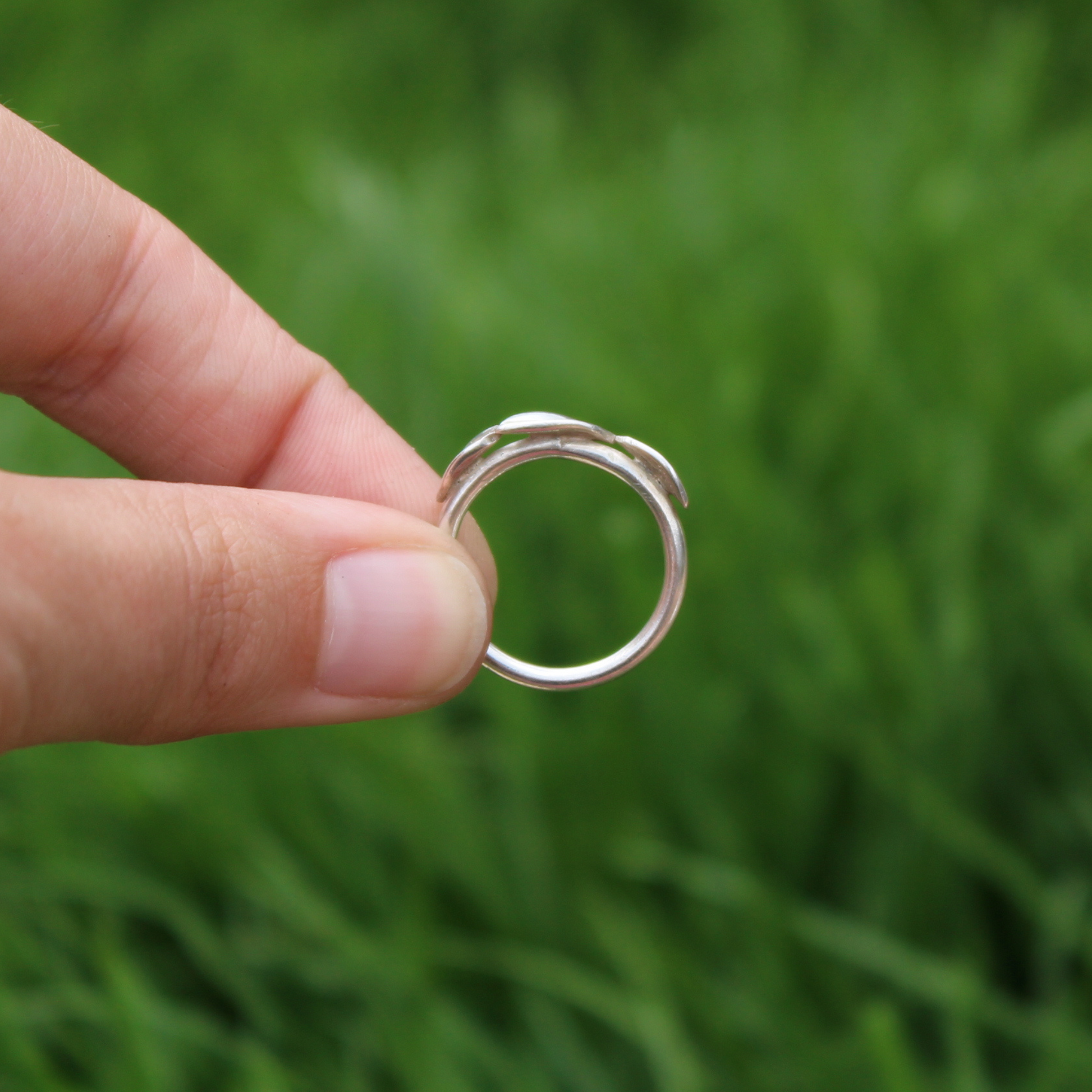 side view of three leaf ring held from the side against a grass backdrop