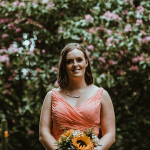 Rachel wearing a peach dress holding sunflowers, wearing a bridesmaid leaf necklace. Leaf background