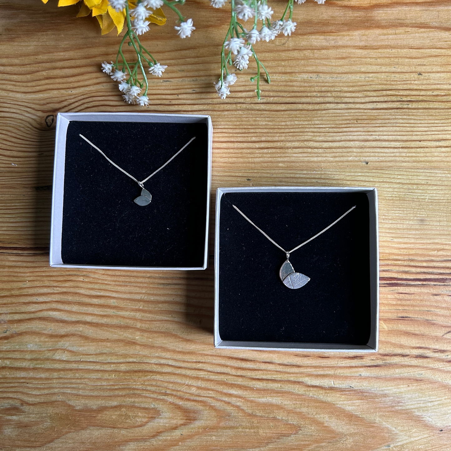 duo leaf necklaces in two sizes in ivory boxes with black insert on a wooden table top