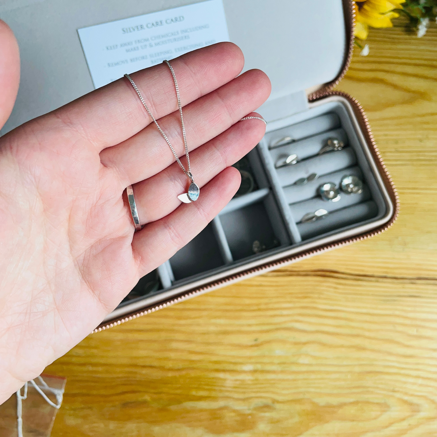 duo leaf necklace in a hand, jewellery box on the table behind