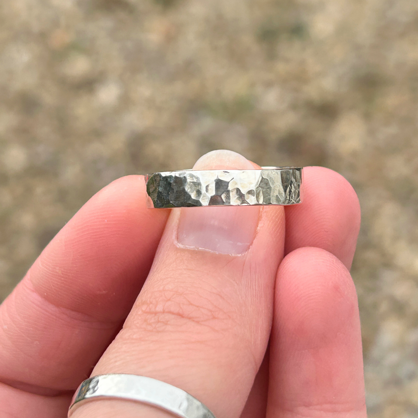 Hand holding a handmade sterling silver ring with a textured band against a blurred natural background