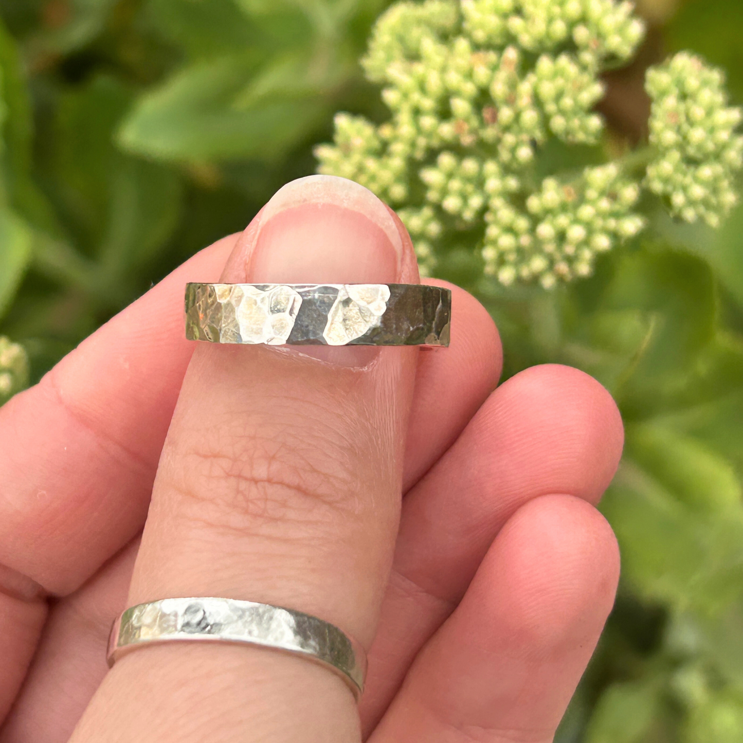 Sterling Silver ring with a textured band held between fingers against a green plant background
