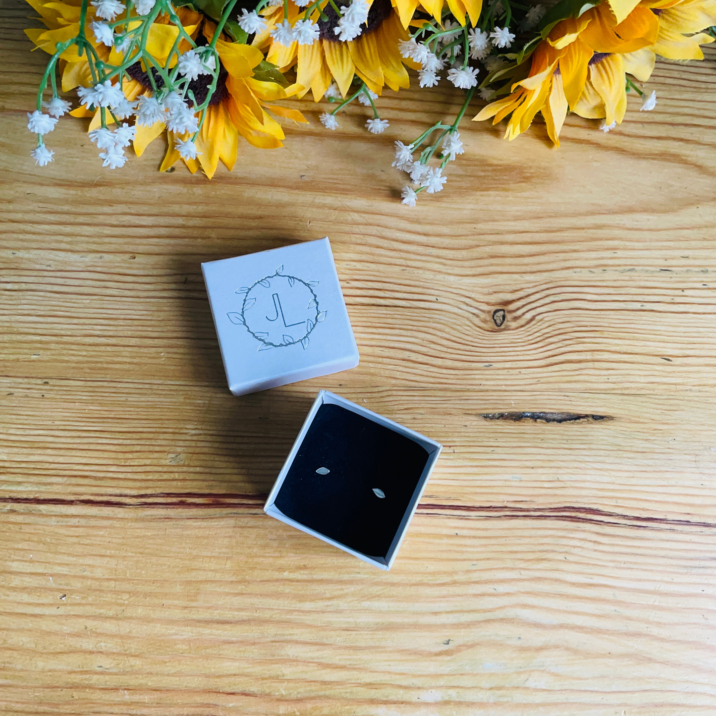 Tiny Flat Leaf Stud Earrings in Sterling silver in an ivory box on a wooden table top handmade by Jen Lithgo Jewellery