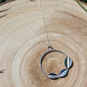 Handmade sterling silver necklace on a wooden background. Three Leaves on a circle hang from a curb chain. Made by Jen Lithgo Jewellery