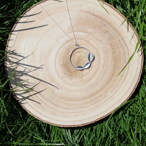 Wooden Log sat in the grass with Sterling SIlver geometric leaf necklace. Handmade by Jen Lithgo Jewellery