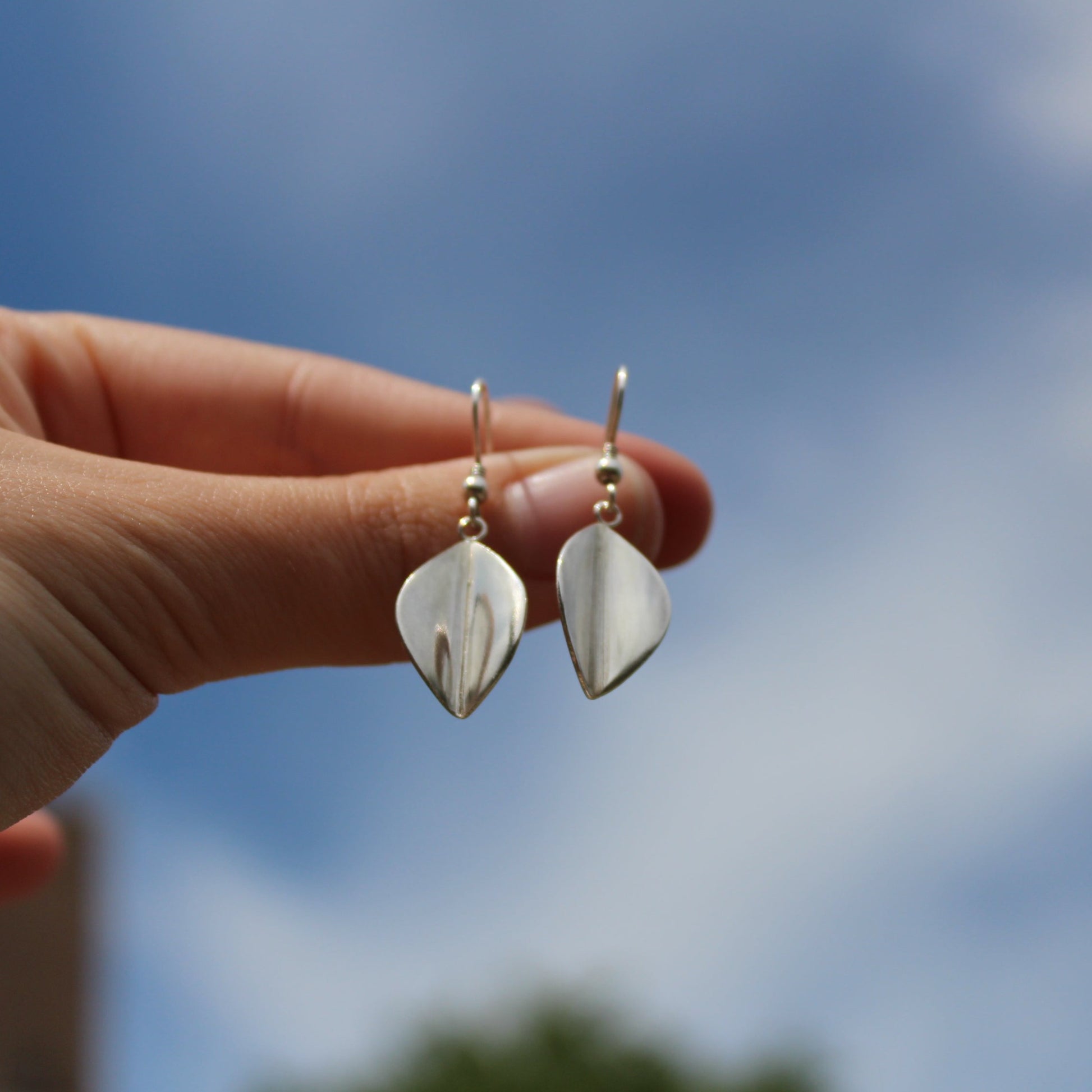 Large Leaf drop earrings being held by a ladies hand towards the sky - Handmade by Jen Lithgo Jewellery