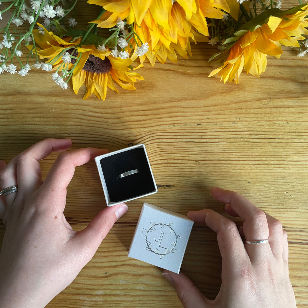 Handemade unisex ring hammered effect 4mm wide displayed in branded ring box held by ladies hands - made by Jen Lithgo Jewellery