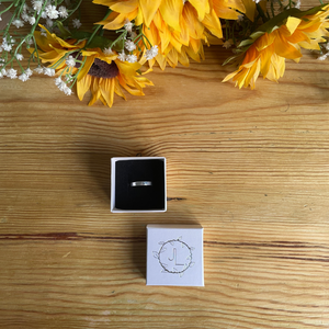 Handmade Hammered 4mm ring in sterling silver sat on a wooden table with sunflowers displayed in a branded box - made by Jen Lithgo Jewellery