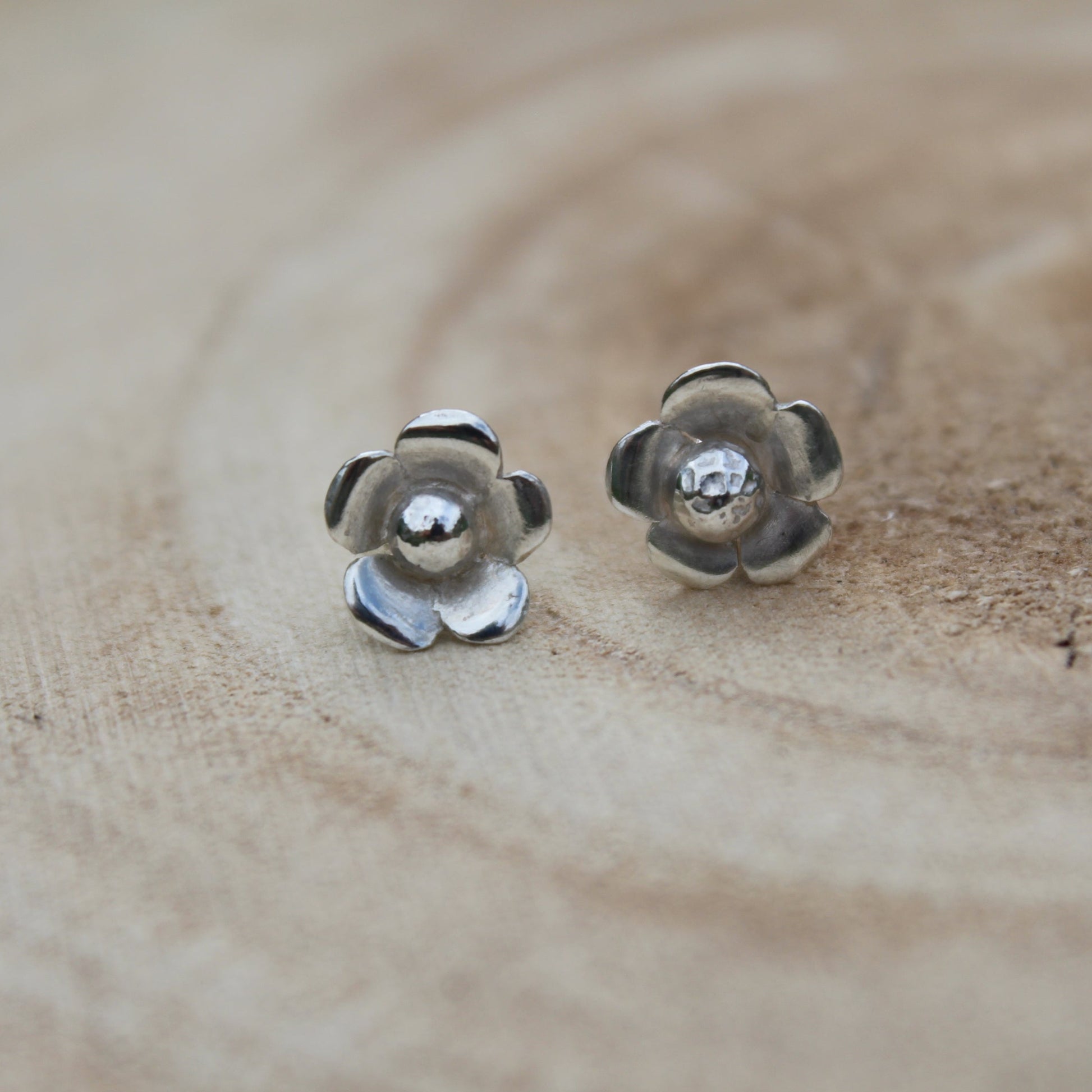A pair of silver flower studs on a wooden background
