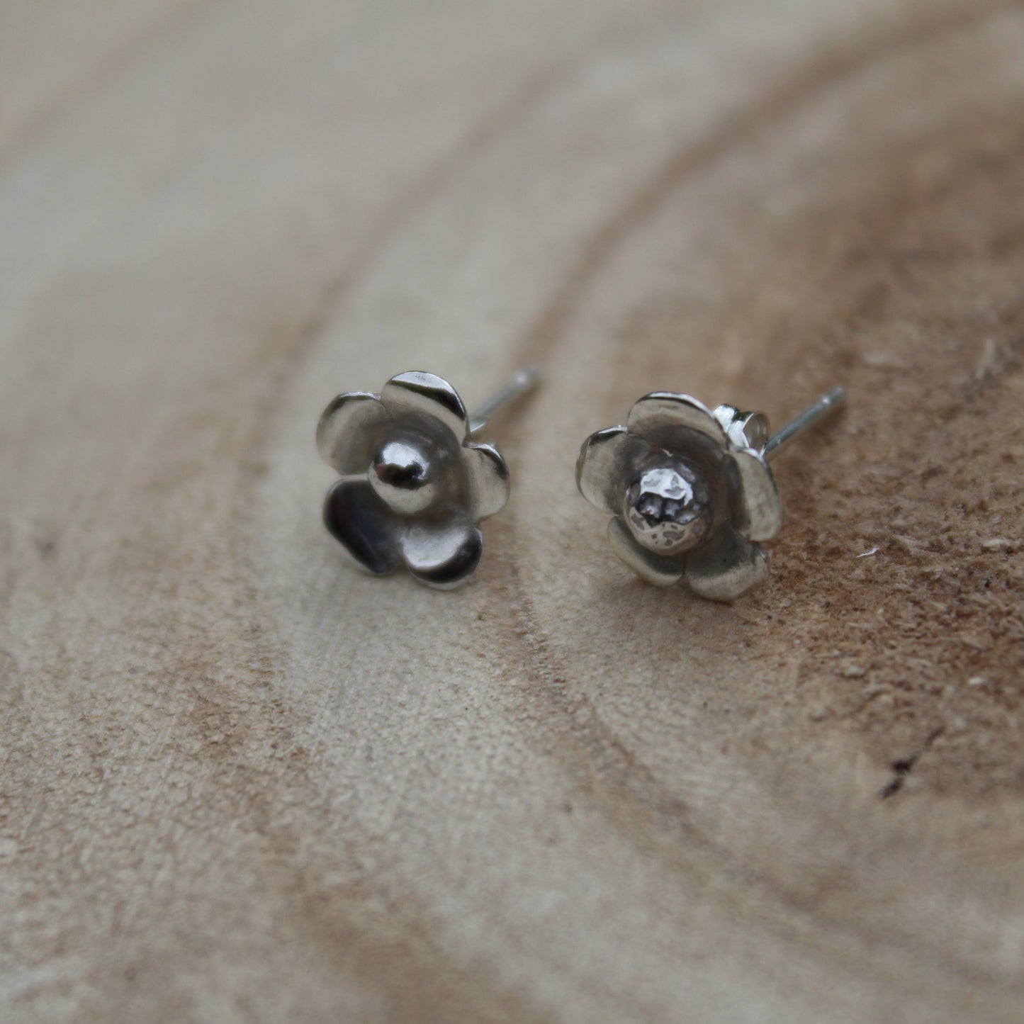 A pair of sterling silver floral stud earrings with a butterfly fastening, displayed on a wooden surface.